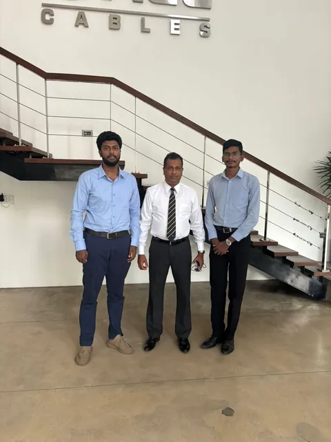 Two members of the team standing with an ACL Cables representative in front of a staircase below the ACL Cables sign in the company's lobby